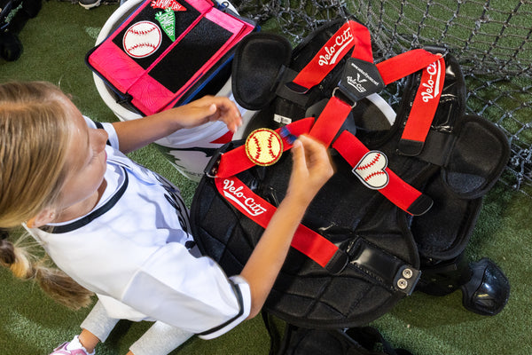 Child interacting with a baseball catcher's gear including a chest protector and leg guards on a grassy field.