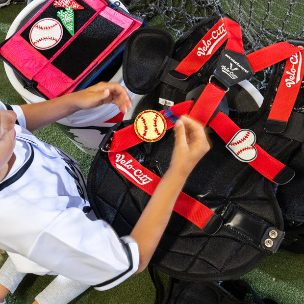 Child interacting with a baseball catcher's gear including a chest protector and leg guards on a grassy field.